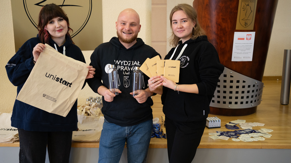 Na zdjęciu znajdują się uśmiechnięci studenci prowadzący szkolenie, którzy trzymają gadżety UniSTART.