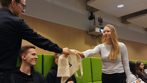 Na zdjęciu znajduje się studentka, której wręczane są gadżety UniSTART.