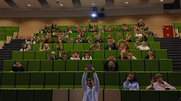 Na zdjęciu znajduje się uśmiechnięta grupa studentów wraz z prowadzącym szkolenie z praw i obowiązków studenta na Wydziale Stosunków Międzynarodowych UwB; wszyscy trzymają podniesione w górę Startery Studenckie.